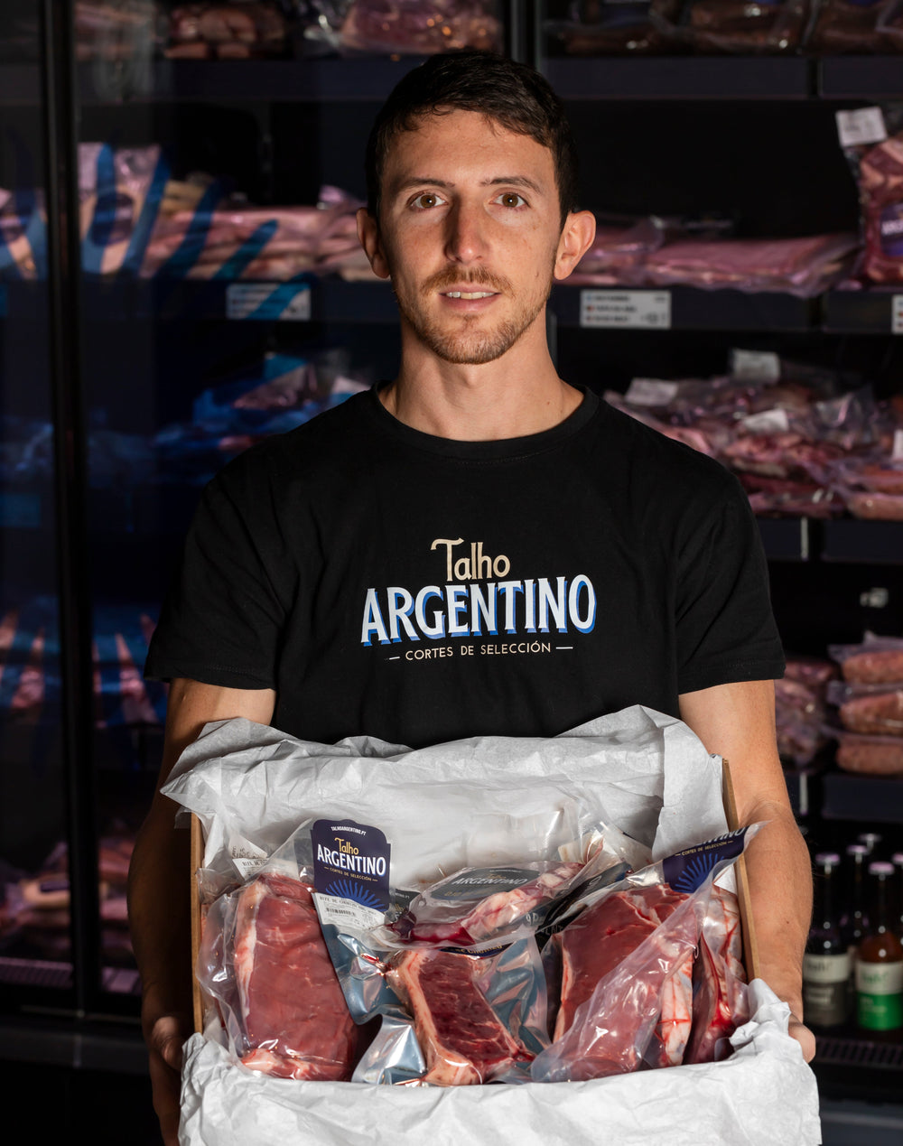Person in a Talho Argentino T-shirt holding a box of vacuum-packed cuts